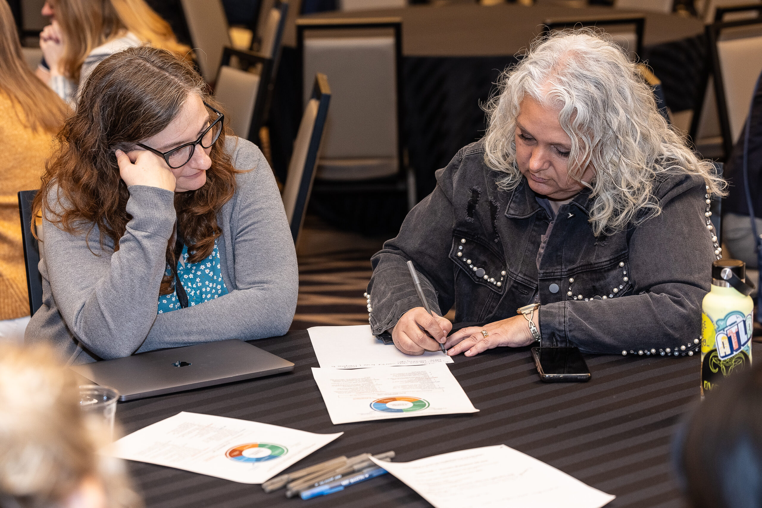 Two white older women looking at a piece of paper on a table and taking notes