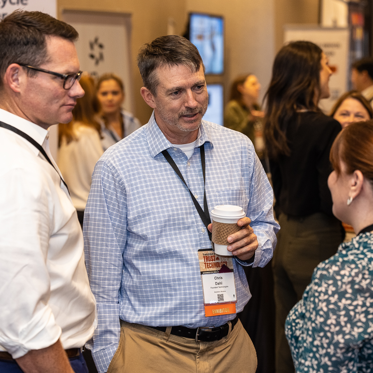 White, middle aged male with light hair holding a coffee and speaking to a middle aged white woman with dark hair.