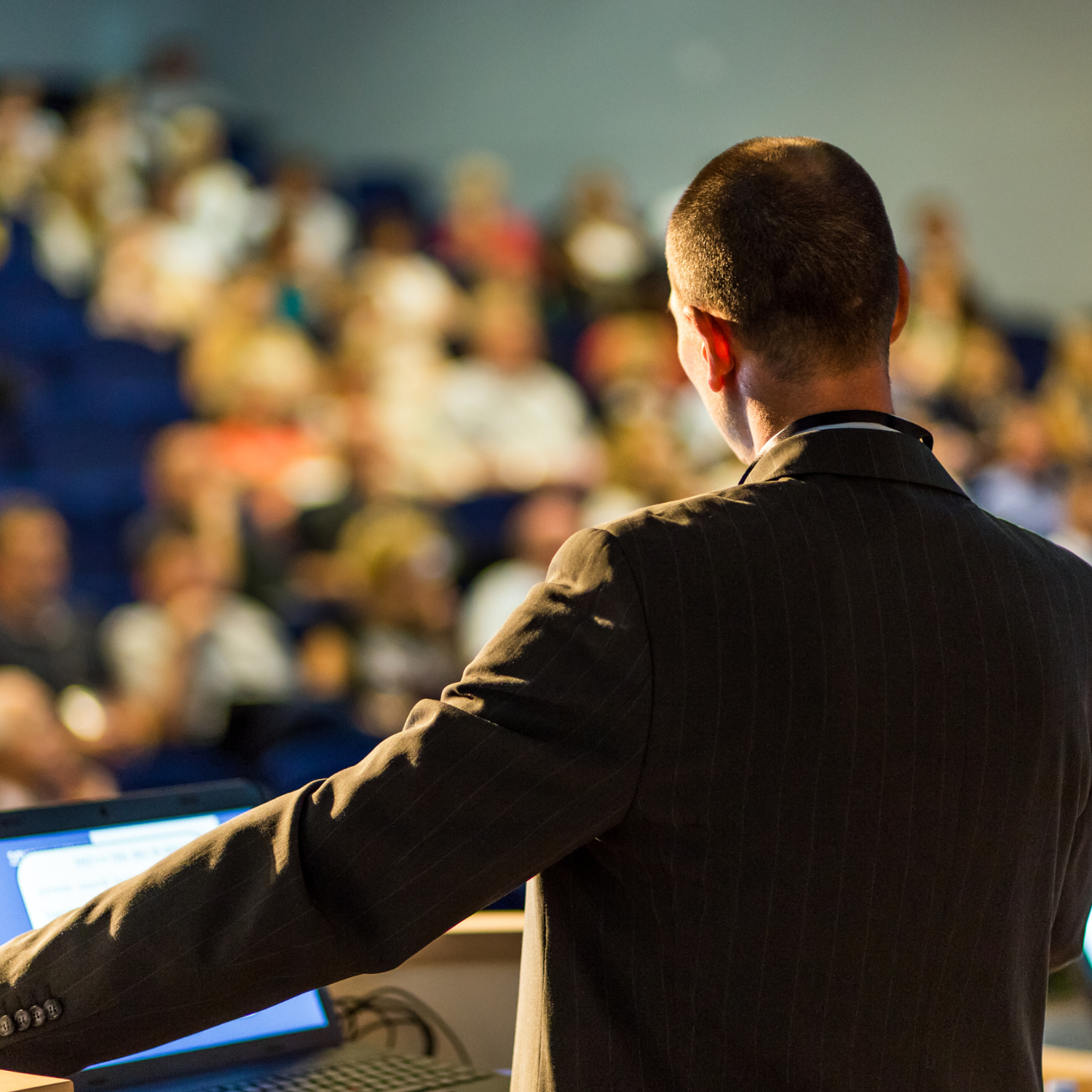 White male with cropped hair overlooks a crowd from behind a podium.