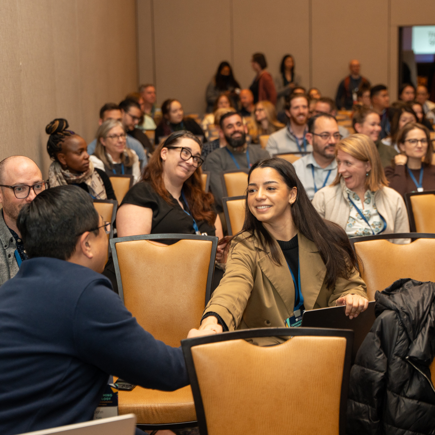 Diverse group of individuals in a conference room, smiling and talking to one another.
