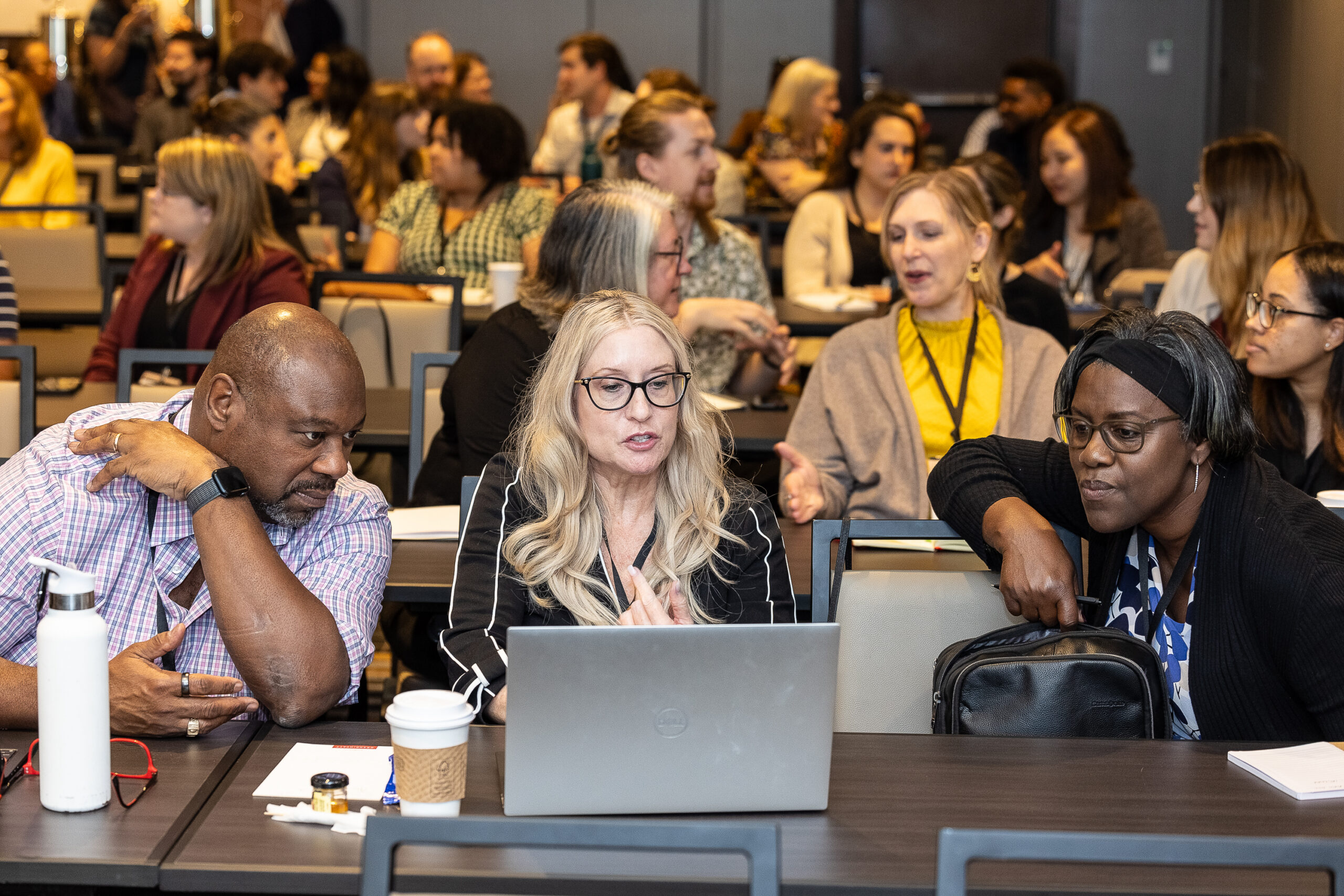 Blonde, white woman sits behind a laptop while a black man and black woman look on from either side of her.