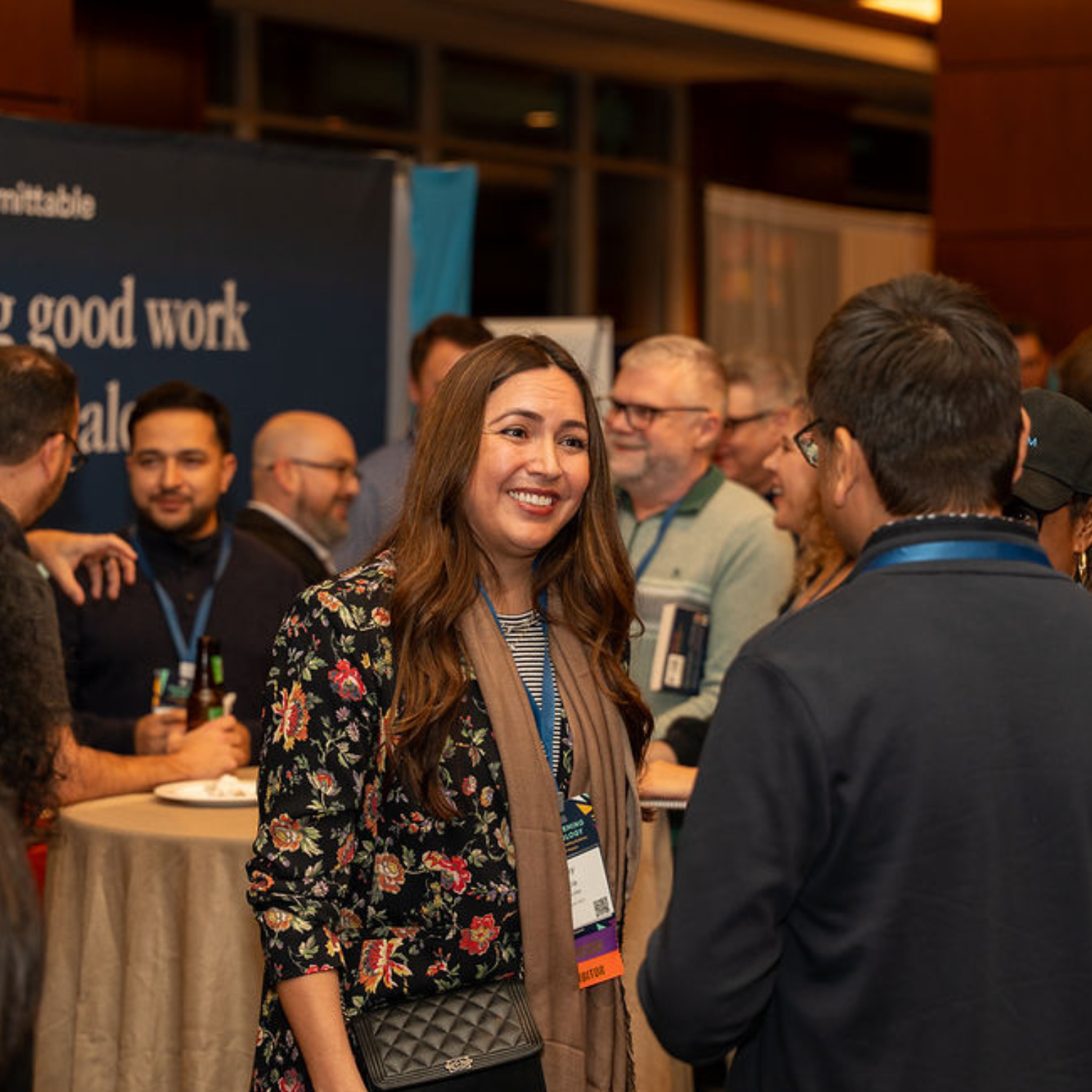 Middle aged woman with medium length brown hair and light brown skin smiling and speaking to a man with short, dark hair and light brown skin.